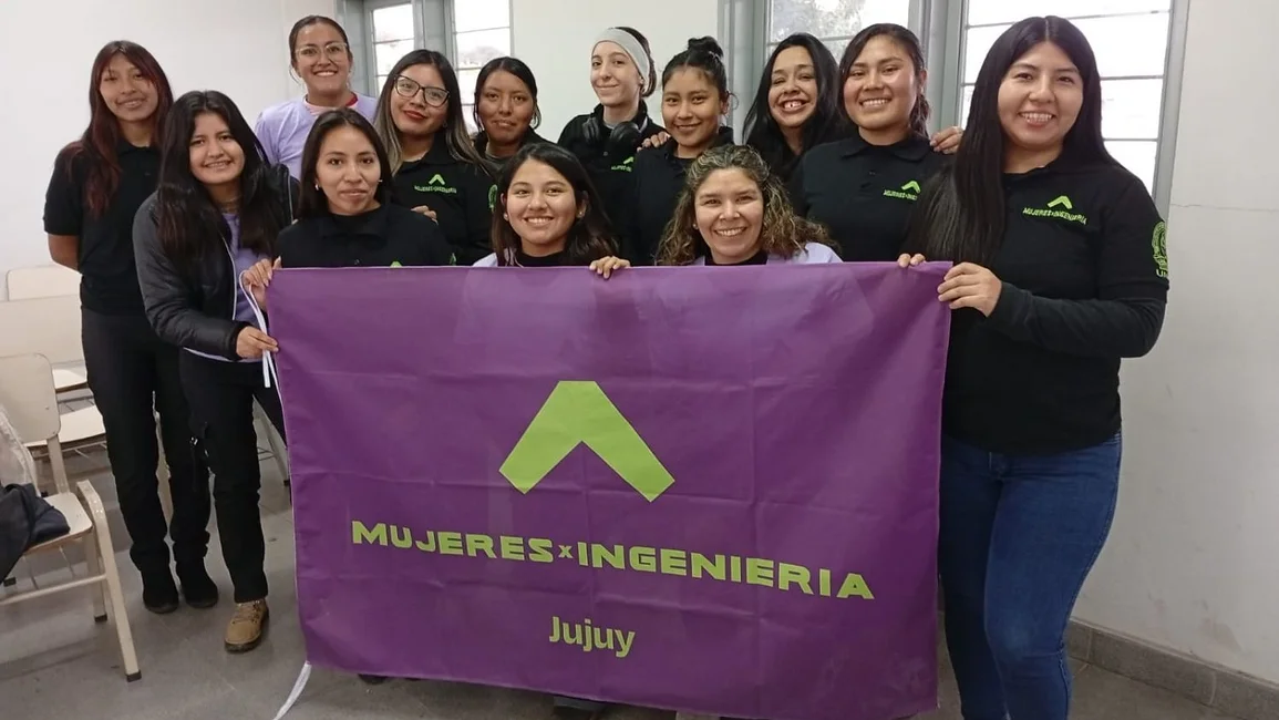 Integrantes de Mujeres x Ingeniería sostienen una bandera violeta de la organización